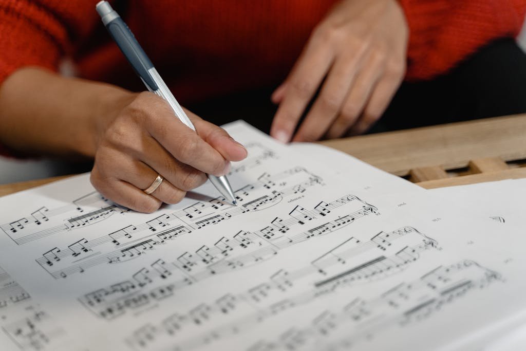 A person writes on sheet music with a pen, focusing on musical notation.