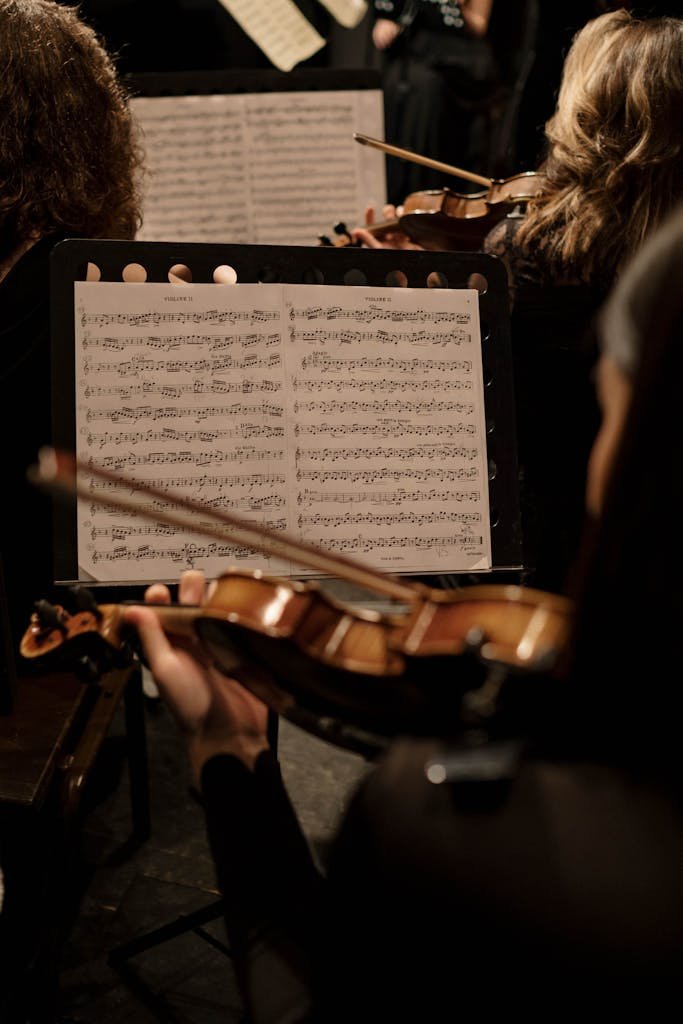 An orchestra violinist during a performance, focusing on sheet music and the instrument.
