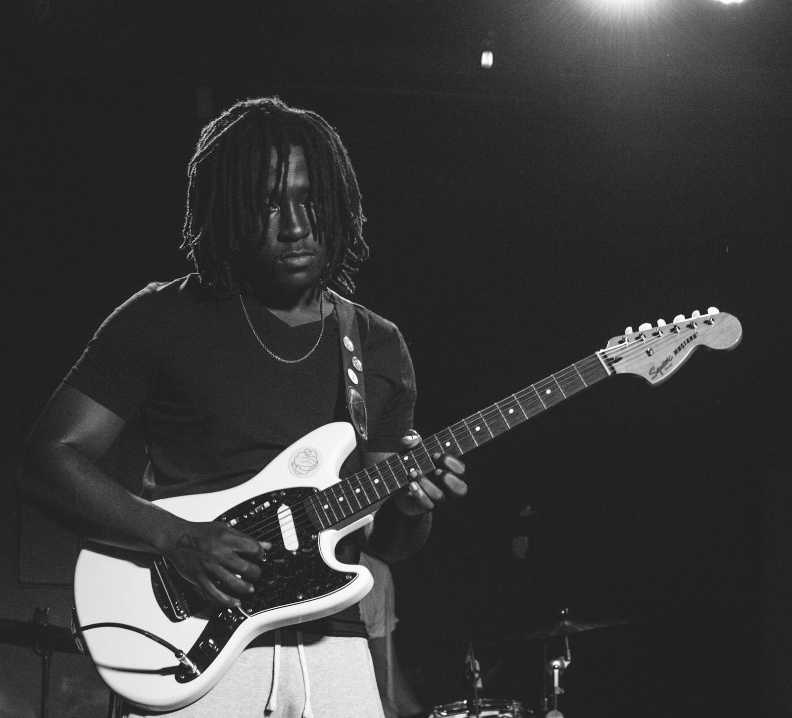 Musician playing electric guitar with stage lights in black and white.