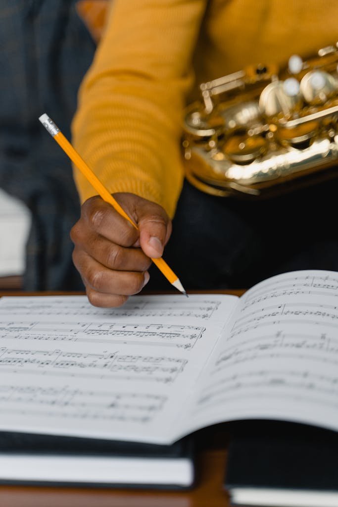 A person writing on a music sheet holding a saxophone, focusing on music composition.